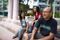 A father and two daughters sit together on a step outside their apartment building. They are smiling and talking. 