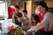 A mother with her three young children roll cookie dough together in their kitchen. The mother is helping the youngest daughter to reach into the bowl to get dough.